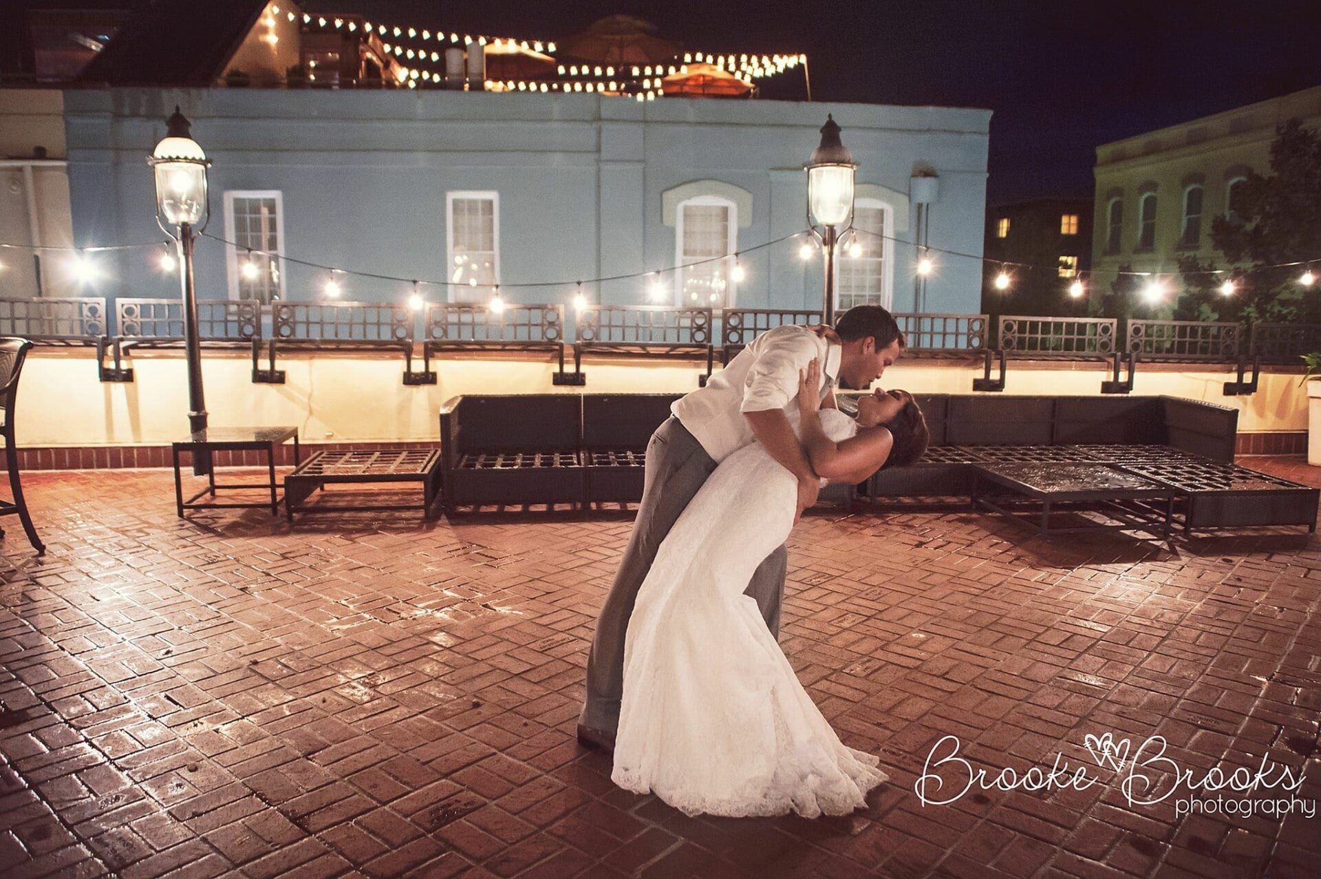 A bride and groom sharing an intimate kiss on a brick patio at night during their Charleston wedding.