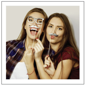 Two women smiling and holding stick props with fake glasses and mustaches to their faces, against a light background.