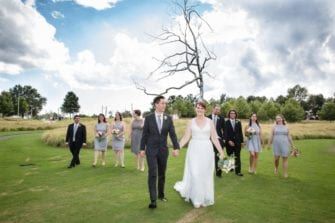 A group of bridesmaids and groomsmen standing in a grassy field.