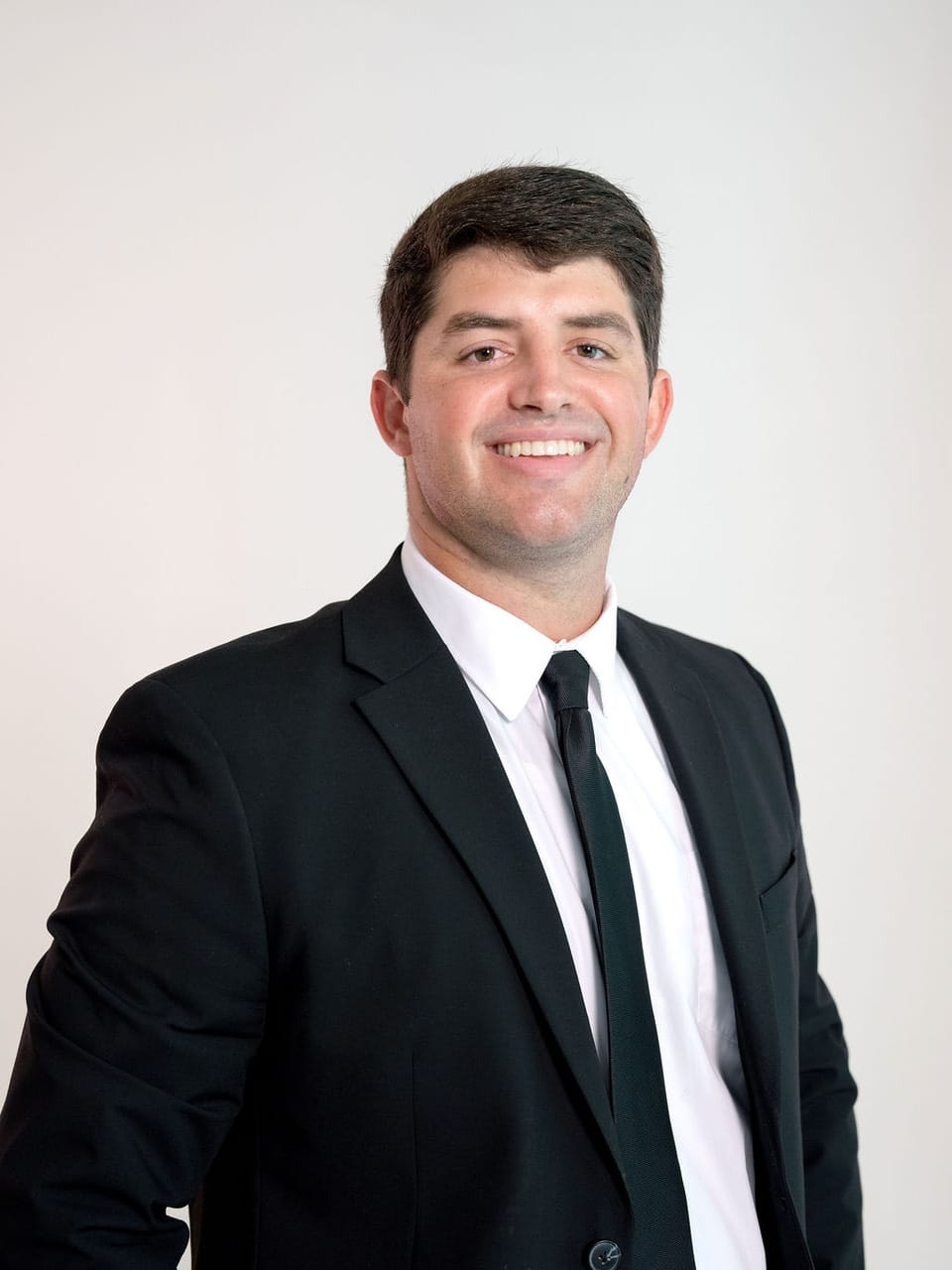 A smiling man in a black suit, white shirt, and black tie.