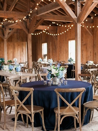 A wedding reception in a barn with blue tables and chairs.