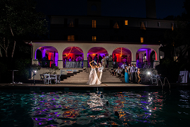 A bride and groom standing in front of a pool at night.