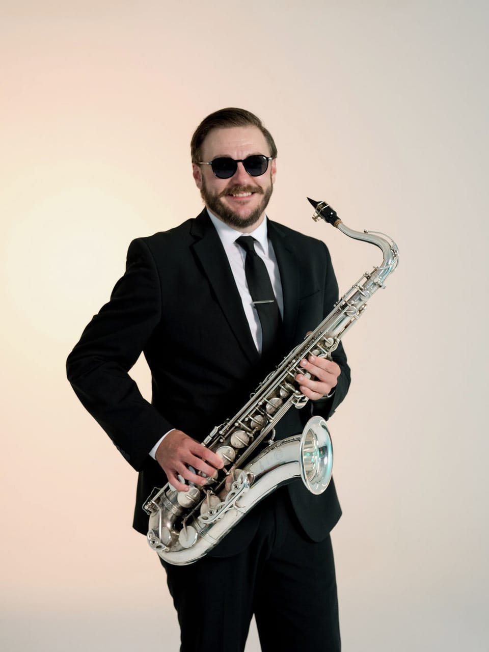A man in a suit and sunglasses holding a saxophone.