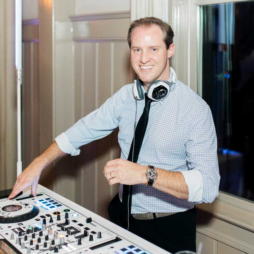 DAVID-FOX-CHARLESTON A man wearing headphones stands behind a DJ console, smiling at the camera in a well-lit indoor setting.