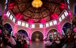 A wedding reception in an ornate building with pink lighting.