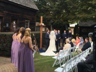 The bride and groom are standing in front of The Sutherland, a wooden building.
