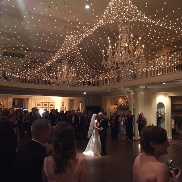A bride and groom standing under a string of lights at their reception in a ballroom.