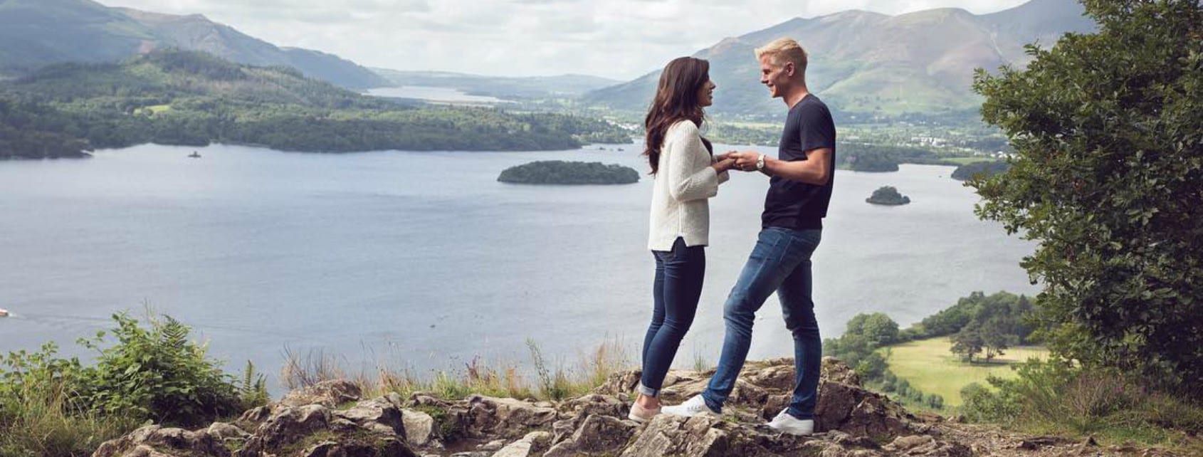 A couple standing on top of a hill overlooking a lake.