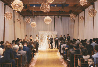 A wedding ceremony in a large room with chandeliers hanging from the ceiling.