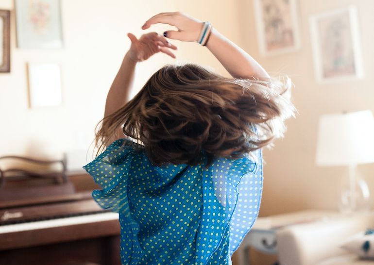 A young girl dancing in front of a piano.