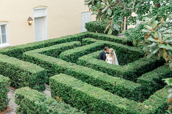 A bride and groom standing in a maze of hedges.