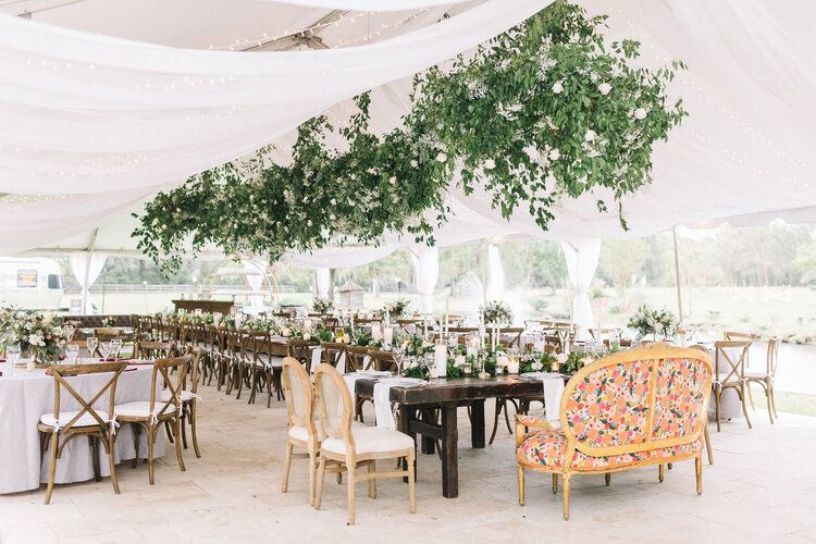 A wedding reception set up in a tent with greenery hanging from the ceiling.