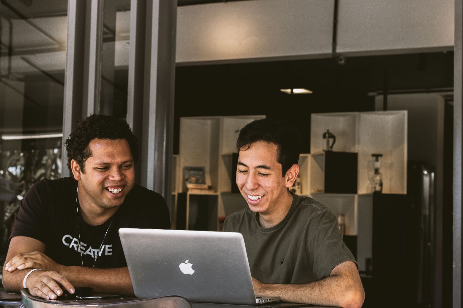 Two men sitting at a table looking at a laptop.