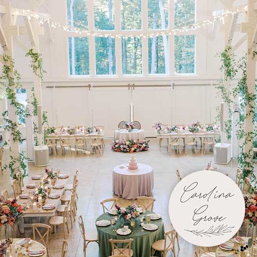 A bright, elegant banquet hall decorated with greenery, round tables set for a formal event, and large windows showing trees outside. A sign reads "Carolina Grove.