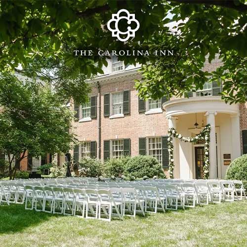 White chairs are arranged in rows on a lawn in front of The Carolina Inn, with greenery and flowers decorating the entrance.