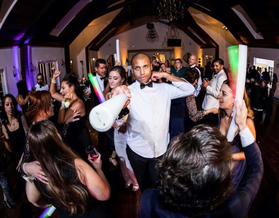richmond-milad-julia A group of people dressed in formal attire dance and celebrate at an indoor party, with one man in the center holding a phone to his ear.