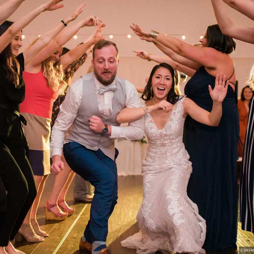 A bride and groom dance enthusiastically under a tunnel formed by guests' raised arms at a wedding reception.