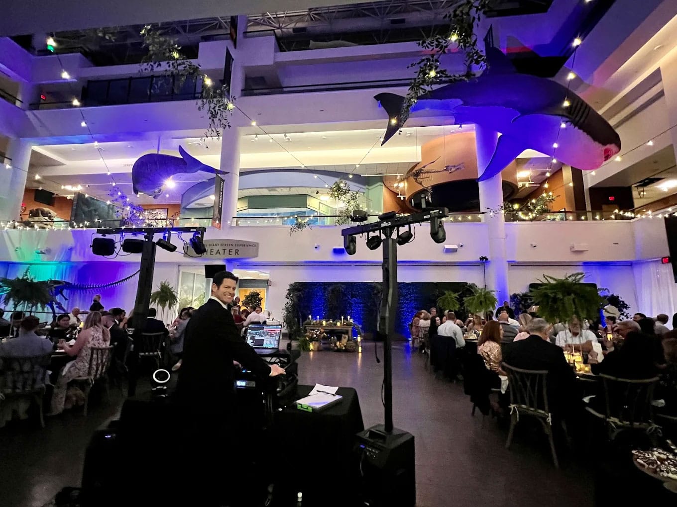 san-diego-event-at-aquarium A banquet event with seated guests, a DJ playing music, and large whale models hanging from the ceiling in a spacious, well-lit venue.