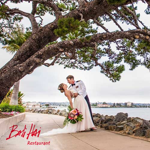 Bali Hai A bride and groom pose under a large tree near the waterfront, with the groom dipping the bride. "Bali Hai Restaurant" logo is visible in the bottom left corner.