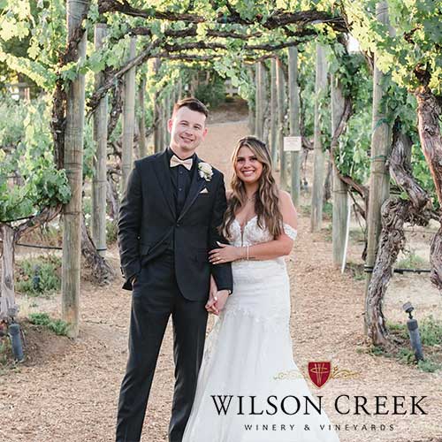 Wilson Creek Winery & Vineyards A bride and groom stand smiling under a grapevine arbor at Wilson Creek Winery & Vineyards.