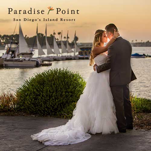 Paradise Point A bride and groom embrace by the water at sunset with sailboats and palm trees in the background; text reads “Paradise Point San Diego’s Island Resort.”.