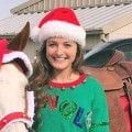 A woman in a santa hat standing next to a horse.