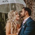 A bride and groom embracing under an umbrella.