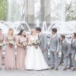 A group of bridesmaids and groomsmen posing in front of a fountain.